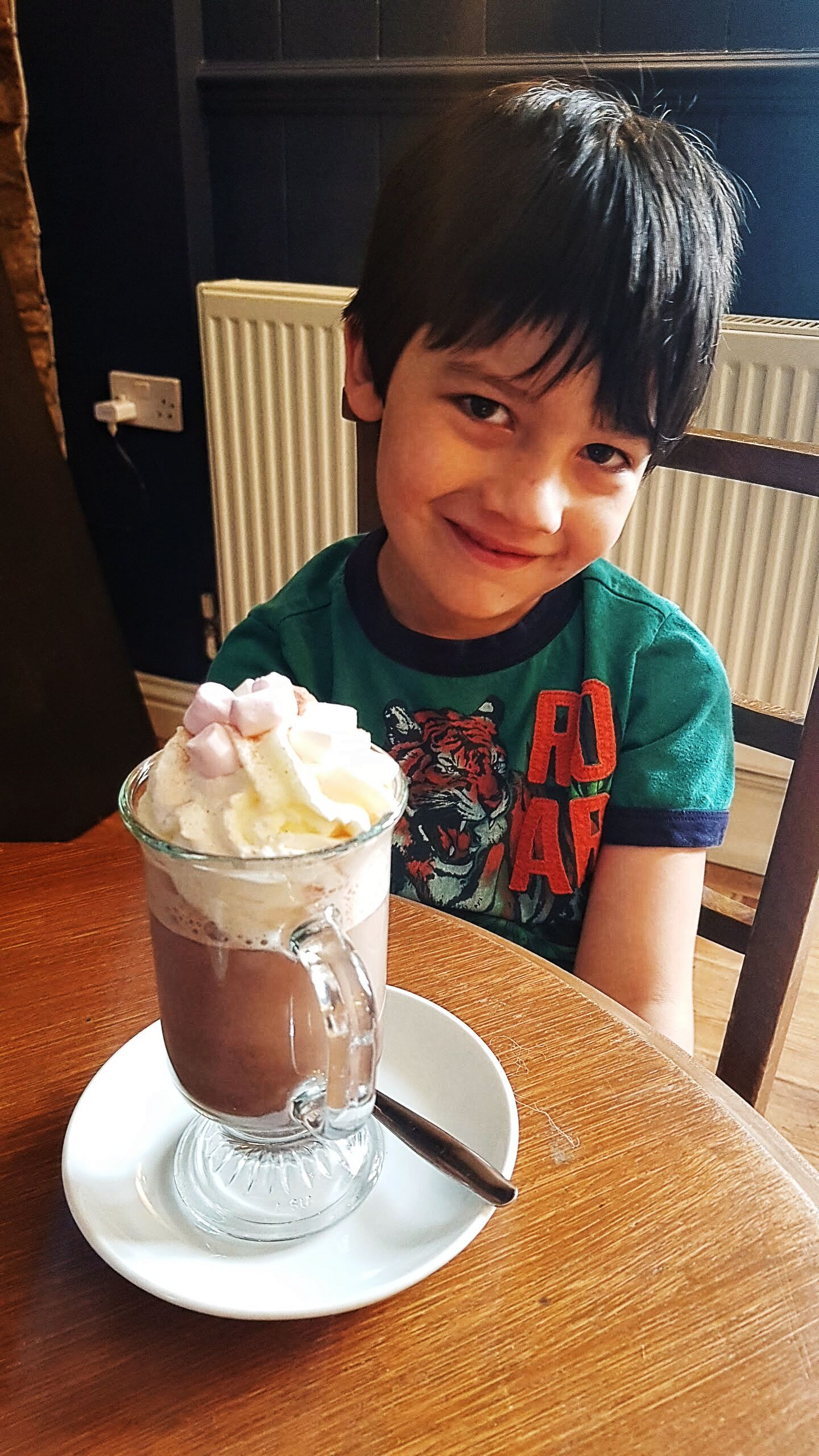 A child sitting at a table with a dessert in a glass cup.