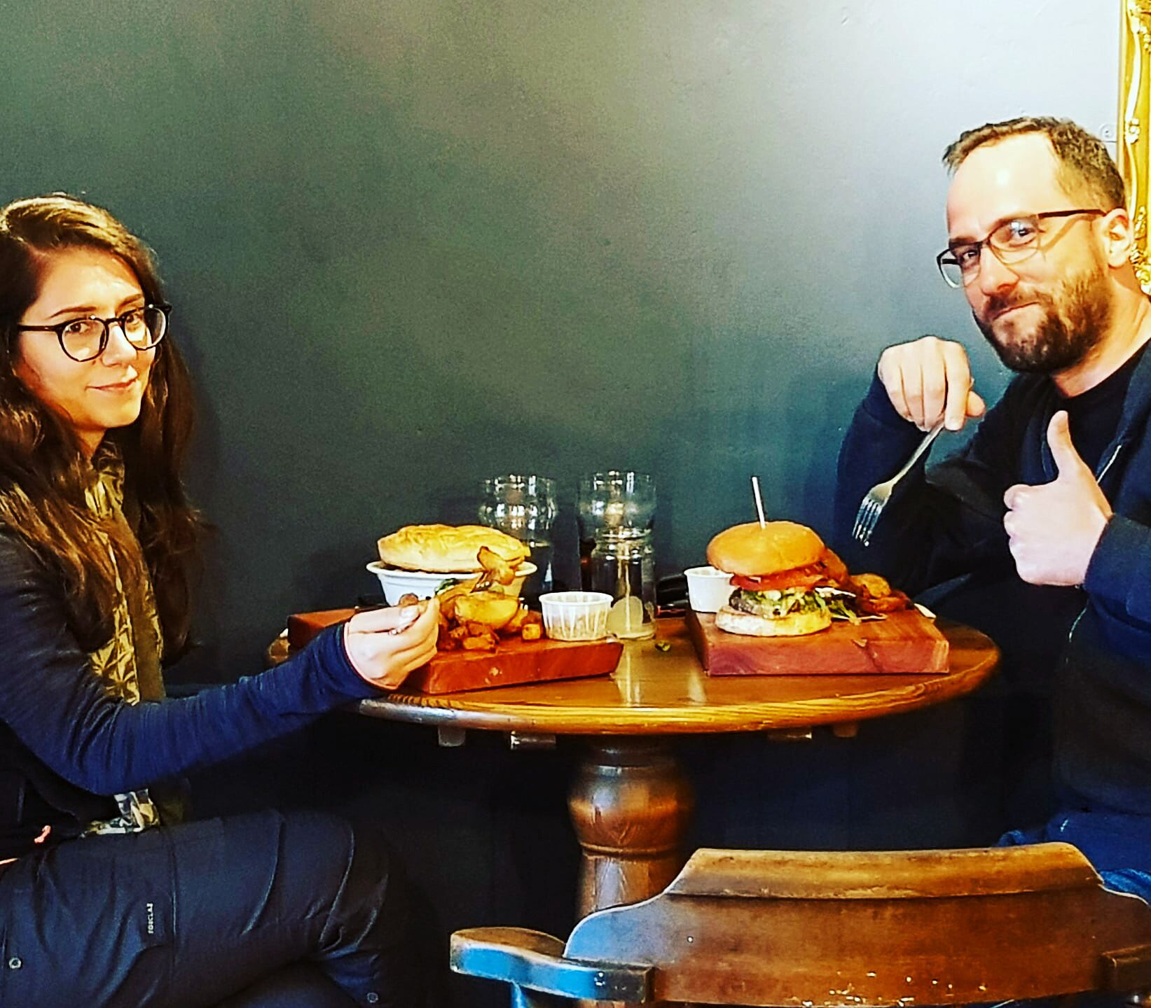 Zwei Personen sitzen an einem Tisch mit Burgern und Getränken.