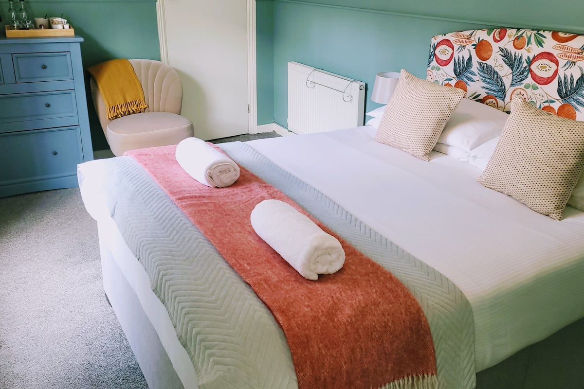 A neatly made bed with a pink and white blanket, two rolled towels, and floral-patterned pillows.