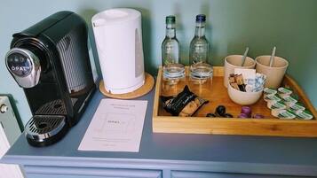 A coffee maker, a white electric kettle, two bottles, two glasses, a tray with cookies, and a bowl with straws and snacks.