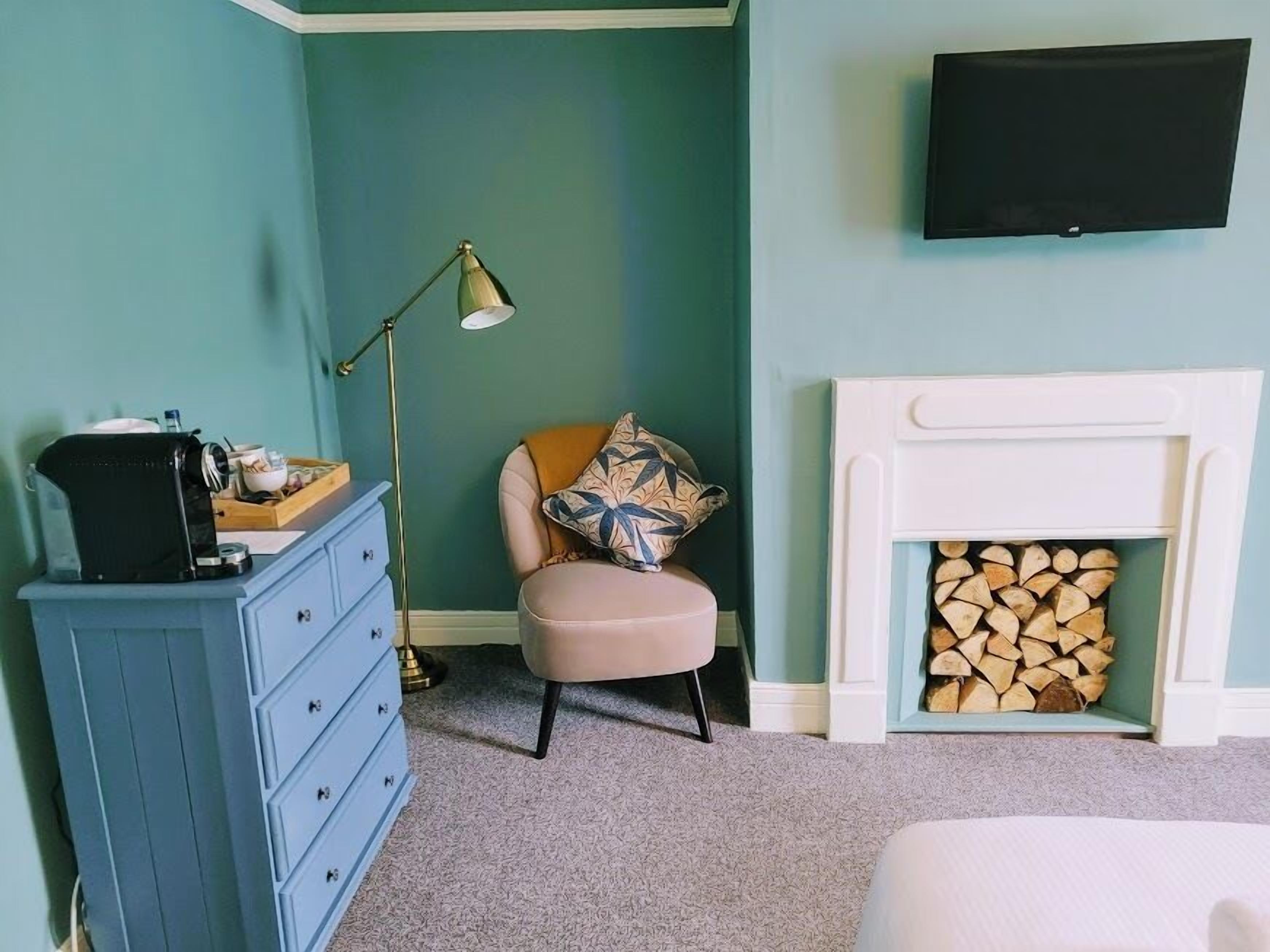A room with teal walls, a white fireplace, a blue dresser, a pink chair, and a flat-screen TV mounted on the wall.