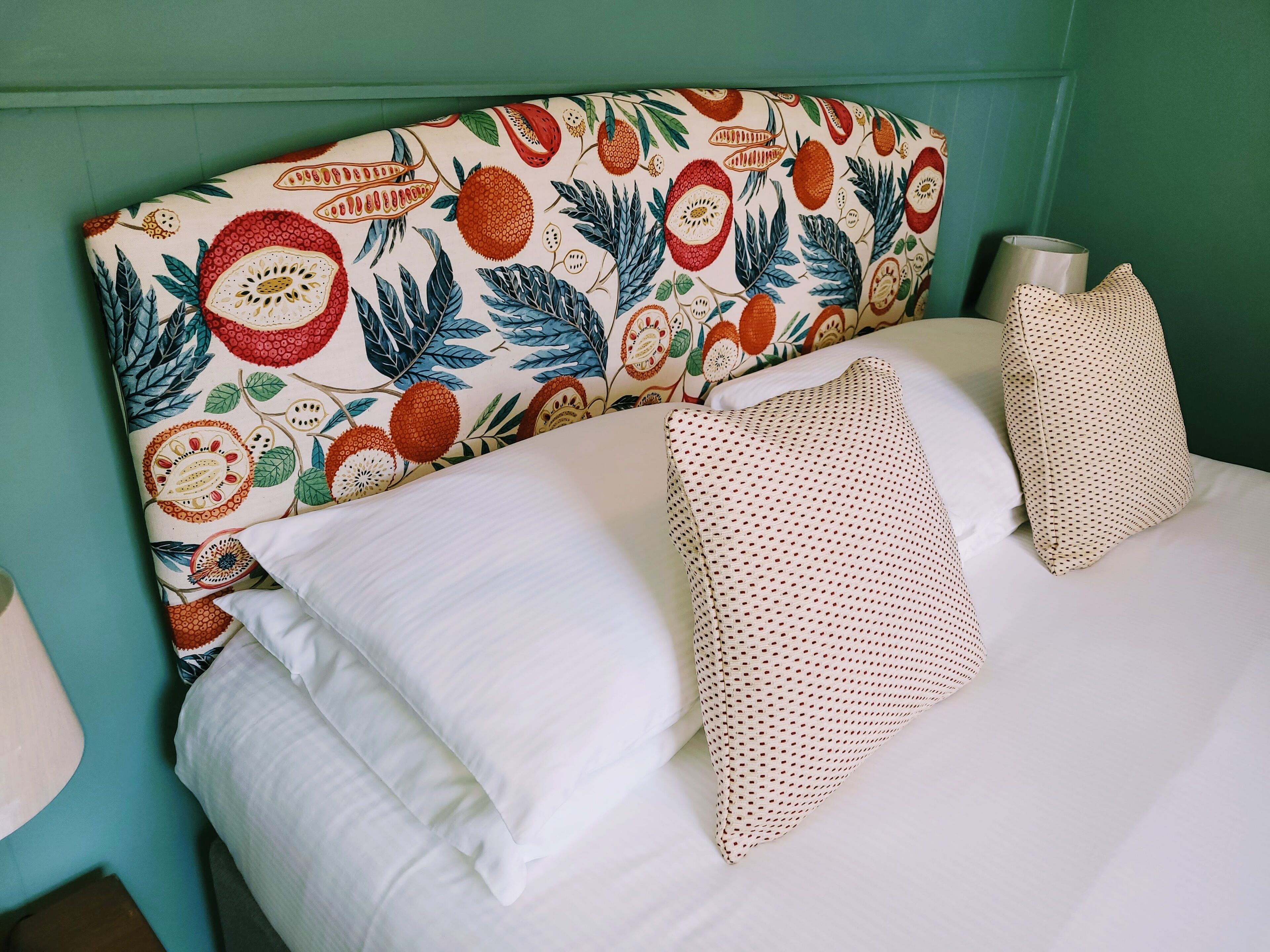 A bed with white linens and a headboard featuring a fruit and leaf pattern.