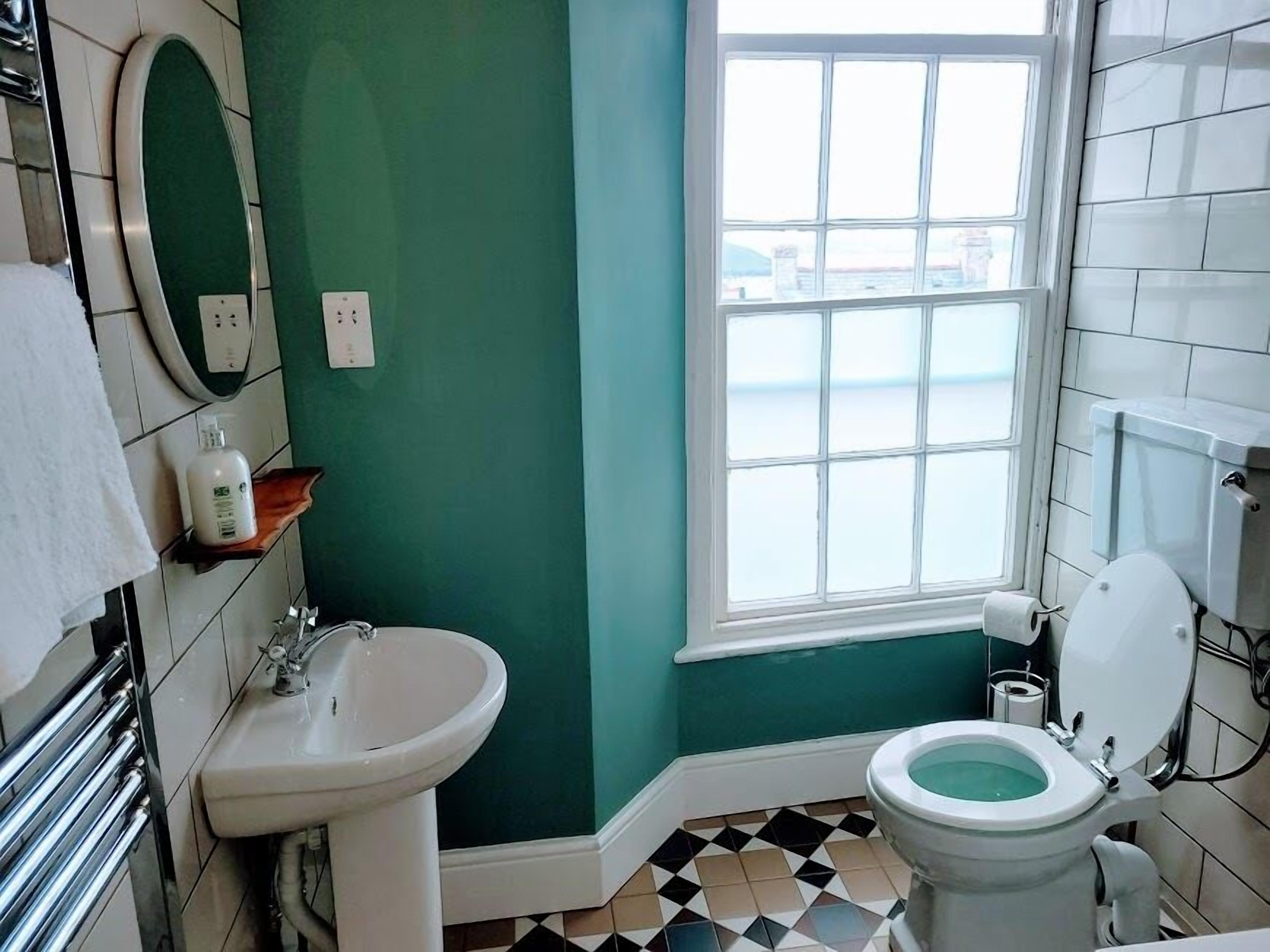A bathroom with a sink, toilet, and a window with a view of the sea.