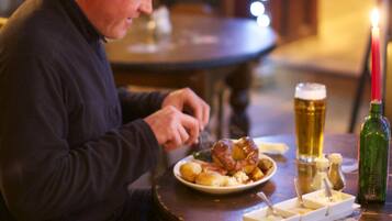 Un hombre sentado a una mesa de madera con un plato de comida, una jarra de cerveza y una vela.
