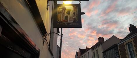 A street view with a pub sign reading "Jacob's Ladder" against a sunset sky.