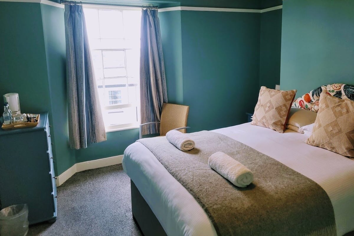 A bedroom with a bed, pillows, a bedside table, and a window with curtains.