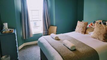 A bedroom with a bed, pillows, a bedside table, and a window with curtains.