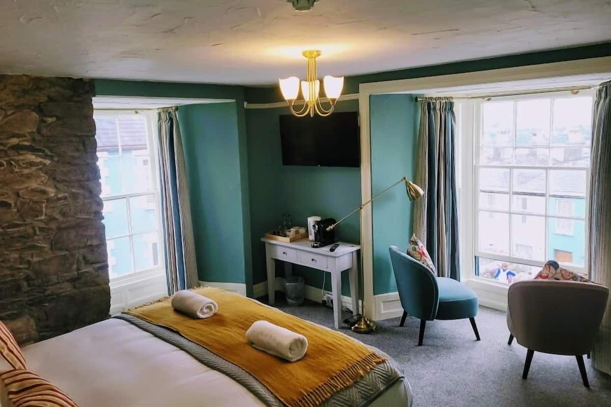 A hotel room with a bed, a desk, a chair, a TV, and large windows.