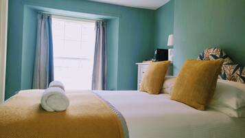 A hotel room with a bed, a window with curtains, a bedside table with a lamp, and a patterned pillow.