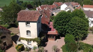Un edificio de estilo europeo tradicional con techo de tejas rojas, rodeado de abundante vegetación y un cielo despejado.