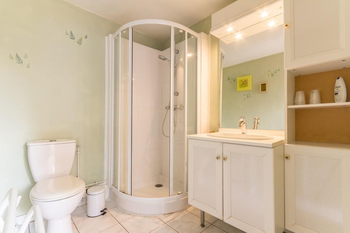 A bathroom with a glass-enclosed shower, a toilet, and a sink with cabinets.
