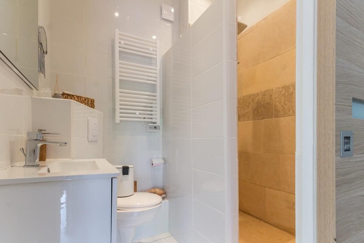 Ein modernes Badezimmer mit Waschbecken, Toilette und Duschbereich, alles in Weiß.