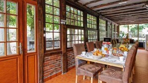 Comedor con pared de ladrillo, ventanas amplias y una larga mesa dispuesta para el desayuno.