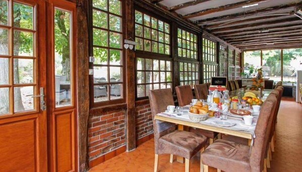 A dining area with a brick wall, large windows, and a long table set for breakfast. - La Pouillyzotte (Pouilly-sur-Loire)