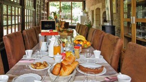 Un desayuno preparado para dos personas, con croissants, fruta y una botella de zumo de naranja.
