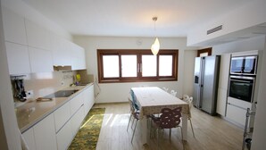 A modern kitchen with white cabinets, a dining table with chairs, a refrigerator, and a microwave. - Villa Franca (San Teodoro)