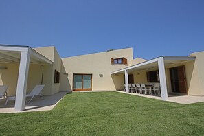 A modern building with a flat roof, a covered patio with white chairs, and a well-maintained lawn. - Villa Franca (San Teodoro)