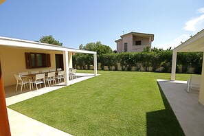 A spacious backyard with a well-maintained lawn, a dining area with a table and chairs, and a covered patio area. - Villa Franca (San Teodoro)