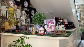 Un mostrador de recepción con un cartel que ofrece un bono de referencia, rodeado de relojes que marcan diferentes ciudades, una planta en maceta y varios objetos decorativos.