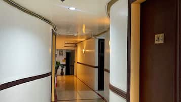 A hotel corridor with a wooden door marked '404' on the right, a white wall with a brown trim on the left, and a tiled floor.