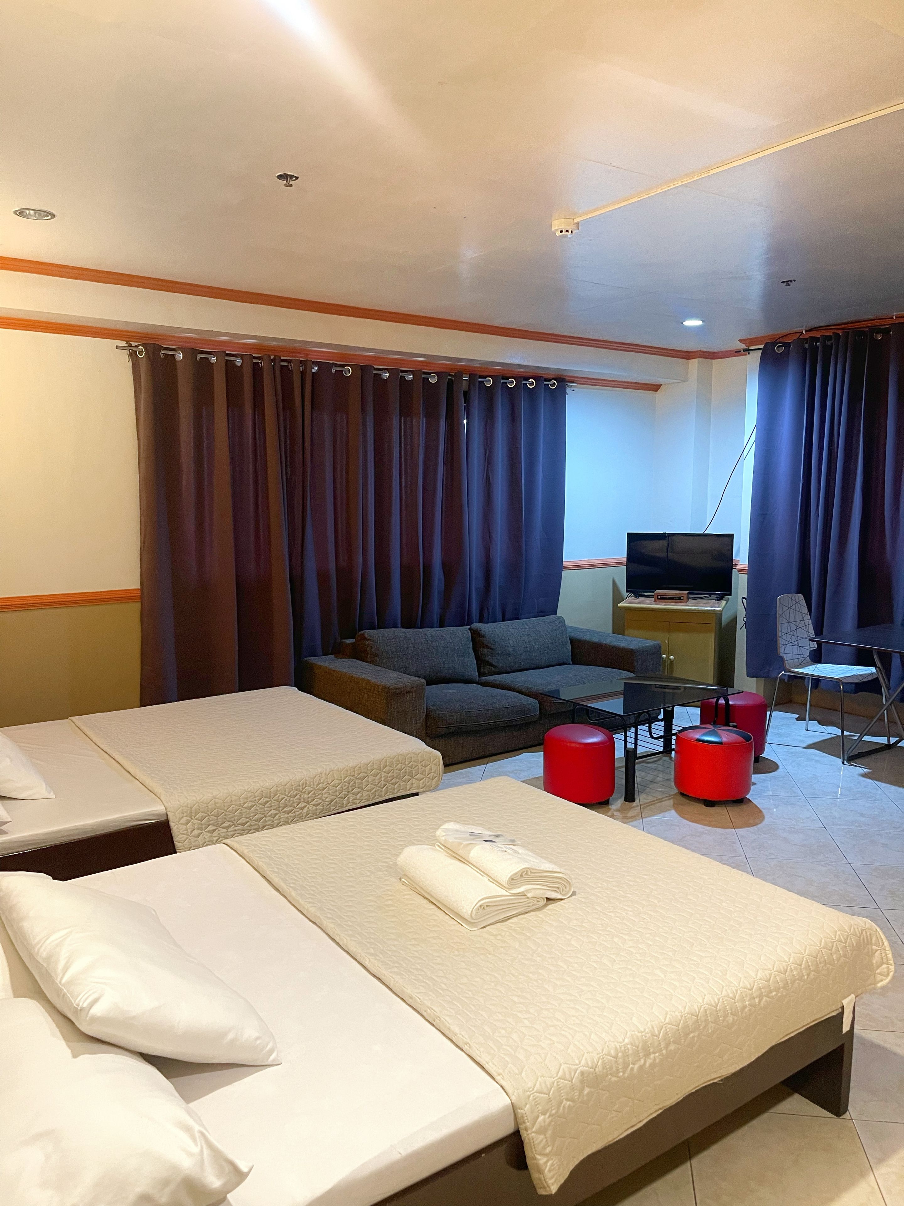A hotel room with two beds, a sofa, a TV, and a desk.