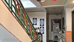 A staircase with green and orange railings, a tiled floor, and a hallway with framed pictures and a vase of flowers. - Tabaco Gardenia Hotel (Tabaco City)