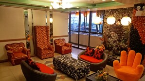 A lobby with patterned armchairs, a hand-shaped chair, and a stone wall with a fire exit sign. - Tabaco Gardenia Hotel (Tabaco City)