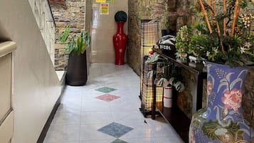 A hotel lobby with a stone wall, a reception desk, potted plants, and a tiled floor.