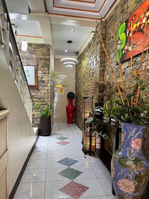 A hotel lobby with a stone wall, a reception desk, potted plants, and a tiled floor. - Tabaco Gardenia Hotel (Tabaco City)