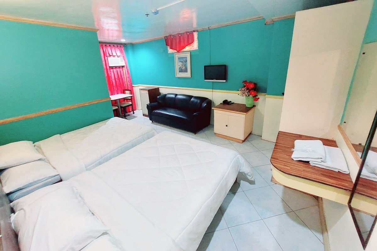 A room with a bed, a desk, a chair, a small cabinet, and a TV on the wall.
