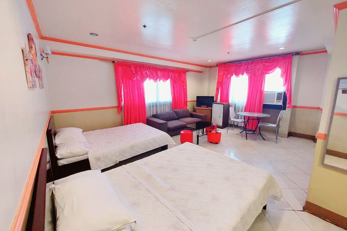 A hotel room with two beds, a sofa, a small table, a TV, and a desk with a chair.