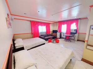 Quarto de hotel com duas camas, um sofá, uma mesinha, uma televisão e uma escrivaninha com uma cadeira.