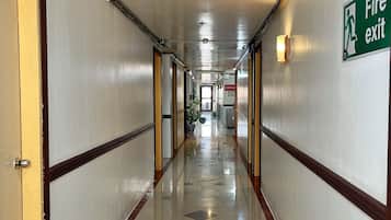 A hotel corridor with a fire exit sign, doors, and a tiled floor.