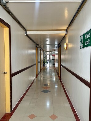 A hotel corridor with a fire exit sign, doors, and a tiled floor. - Tabaco Gardenia Hotel (Tabaco City)