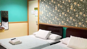 A hotel room with two single beds, a wooden headboard, a green floral wallpaper, and a small desk with a telephone.