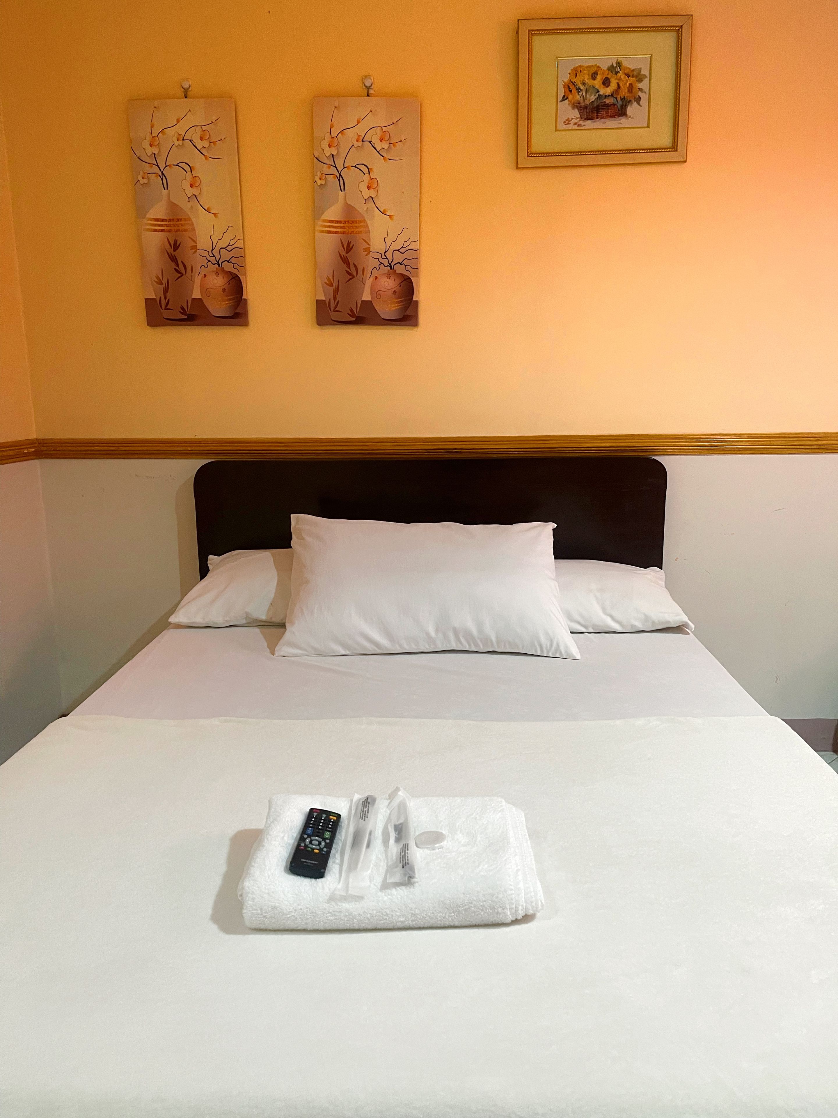 A hotel room with a bed, white bedding, a remote control, and a towel on the bed.