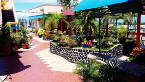 A courtyard with a stone wall, potted plants, and a blue canopy. - Tabaco Gardenia Hotel (Tabaco City)