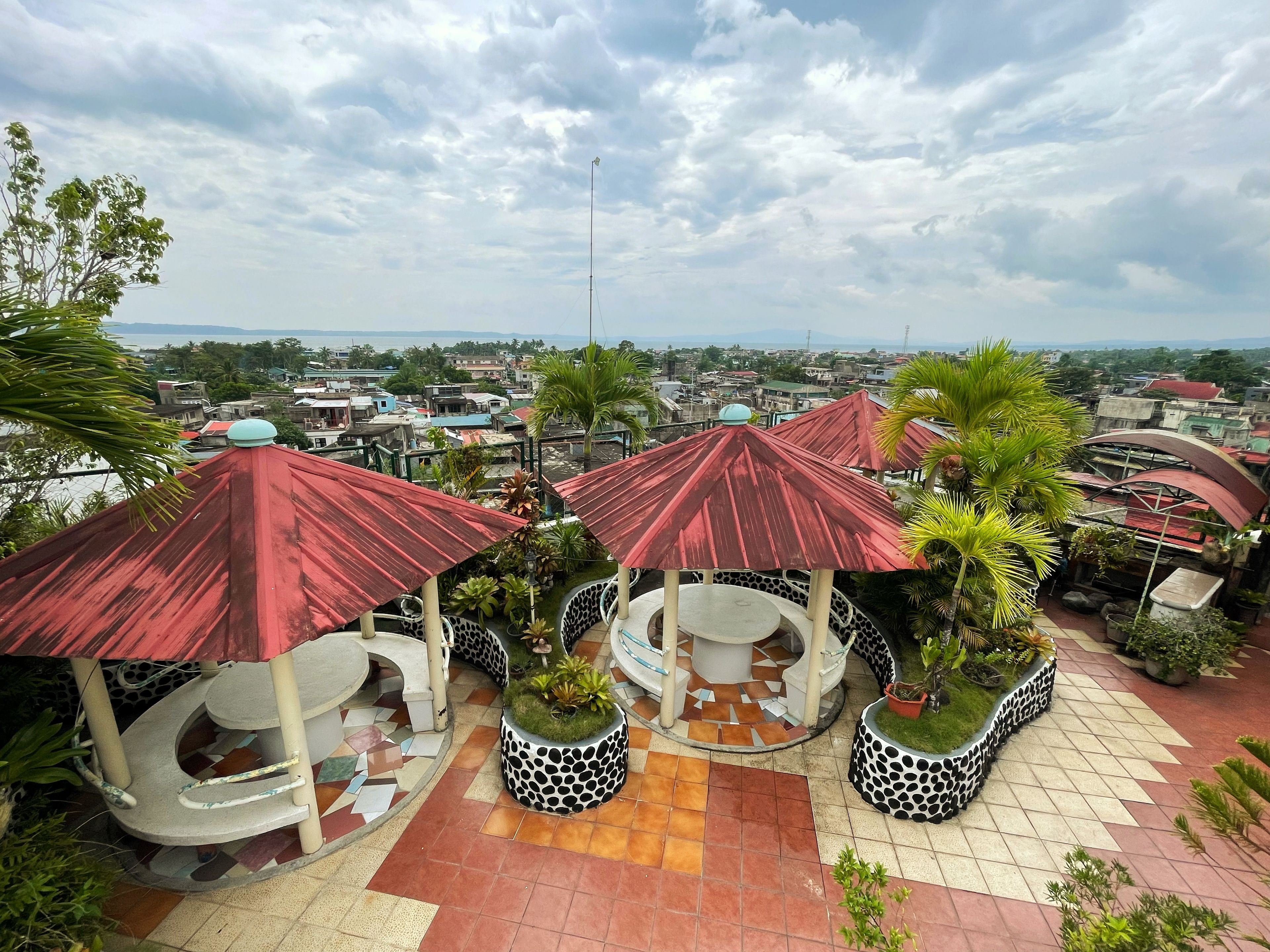 A rooftop garden with multiple gazebos, potted plants, and a tiled floor.