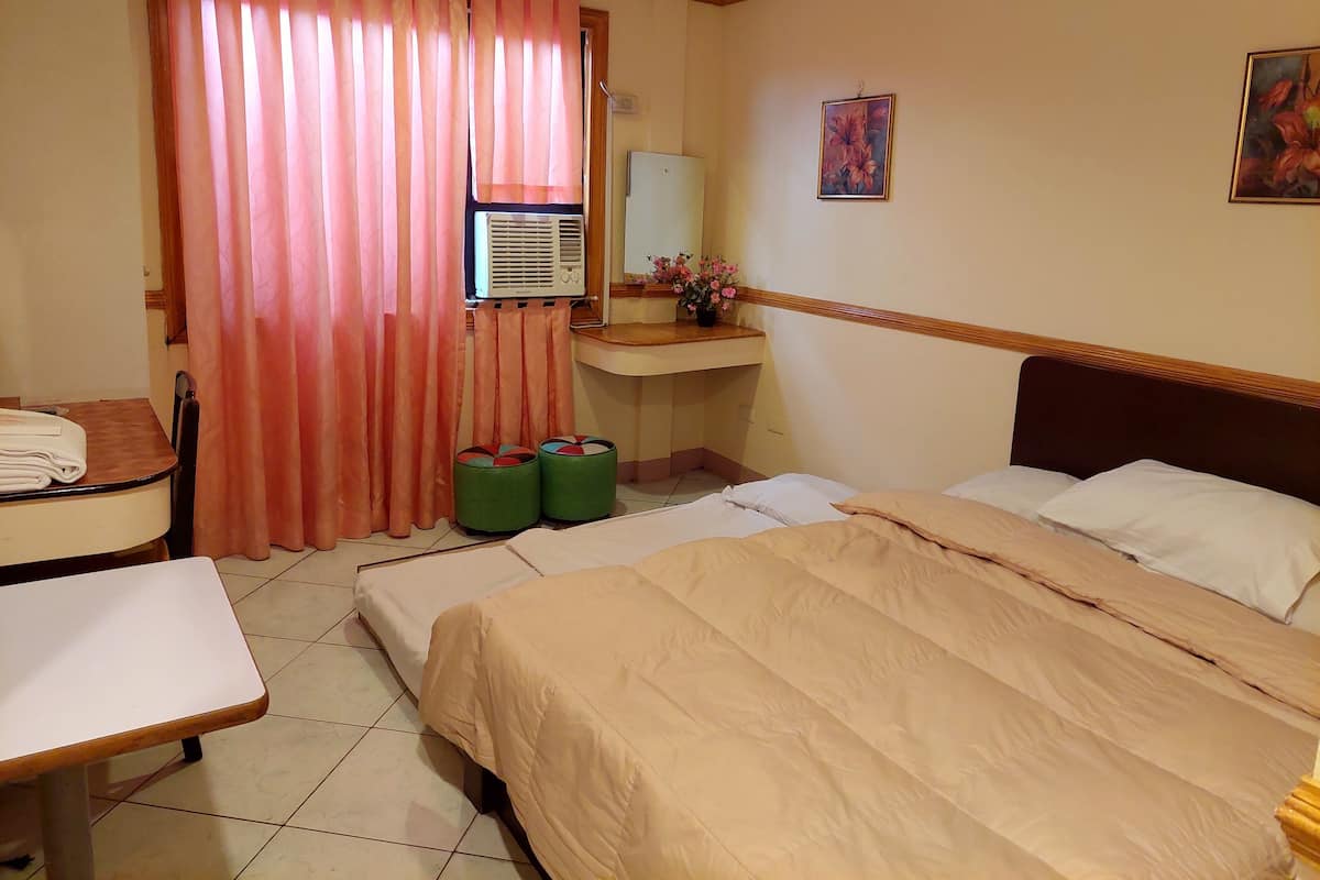 A hotel room with a bed, a desk, a chair, a small table, a sink, and a window with curtains.