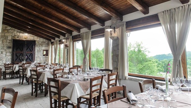 Un restaurant aux murs de pierre, aux poutres en bois et aux grandes fenêtres donnant sur une zone boisée.