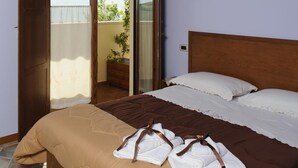 Une chambre avec un plafond en bois, un lit avec une tête de lit marron, un banc et une porte-fenêtre coulissante donnant sur un balcon agrémenté d’une plante.