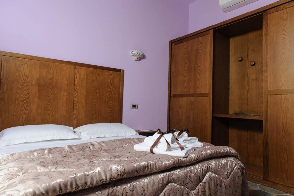Ein Schlafzimmer mit einem hölzernen Kopfteil, einem Bett mit gemusterten Textilien, einem Nachttisch und einem Kleiderschrank.