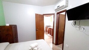 Une chambre à coucher comprenant un lit, une armoire en bois, un appareil de climatisation et un téléviseur fixé au mur.