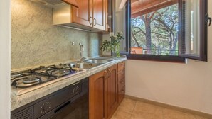 A kitchen with granite countertops, wooden cabinets, a gas stove, and a window with a view of trees. - Villa Corallo (Pula)