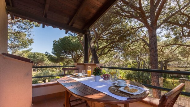 A wooden table set on a balcony with a view of trees, a bottle of orange juice, and a plate with food. - Villa Corallo (Pula)