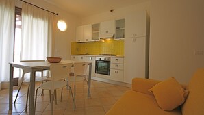 Une cuisine de taille réduite avec des meubles blancs, un pare-feu jaune et un coin repas comprenant une table et des chaises.