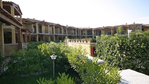 Une cour bordée d’immeubles à plusieurs étages, un jardin central agrémenté de diverses plantes et un lampadaire.