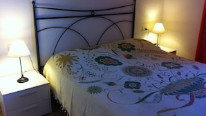 Un lit recouvert d’une couvre-lit à motifs floraux, deux lampes de chevet, une table de chevet blanche avec des tiroirs et une tête de lit en métal noir.