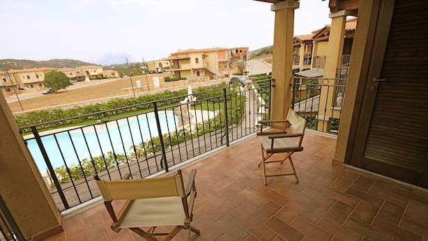 Un balcon avec deux chaises en bois, une piscine et une vue sur des immeubles d’habitation.