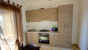 A compact kitchen with wooden cabinets, a gas stove, a dishwasher, and a small countertop. - Myrsine 2 (Olbia)